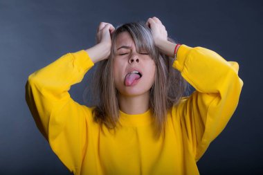 Güzel bir genç kadının siyah arka plan üzerine stüdyo portre. Gözleri kapalı, gözleri kapalı, kafasını iki elle tutarak ile dil gösterir