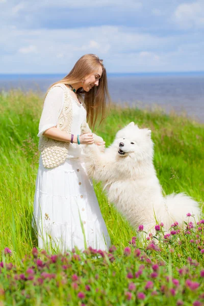 Młoda piękna kobieta stojąc z duży biały pies kudłaty na tle rzeki w zielonej trawie — Zdjęcie stockowe