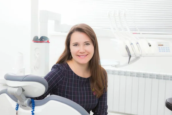 Jonge vrouwelijke patiënt zit op stoel in tandheelkundige office.preparing voor tandheelkundige examen. Kijken naar camera. — Stockfoto