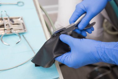the dentist prepares a latex scarf with metal clips for the treatment of canals and pulpitis. Pliers punches a hole in the latex insulating napkin clipart