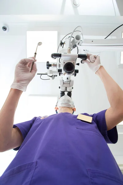 Dentista maschio che indaga sul microscopio binoculare endodontico dentale professionale con fotocamera nello studio. vista dal basso — Foto Stock