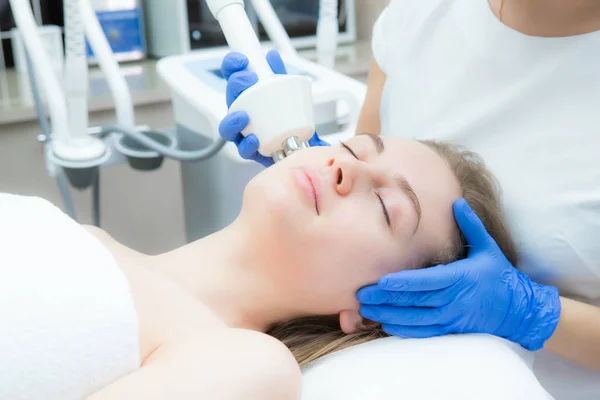 Una giovane bella donna riceve un massaggio facciale elettrico su attrezzature di bellezza. Cosmetico in guanti. Cosmetologia moderna — Foto Stock