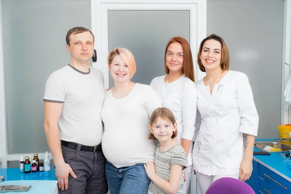 Famiglia felice - papà, figlia, madre incinta con due giovani bei medici in una clinica medica. Tutti guardano la cornice. — Foto Stock