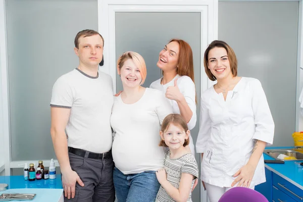 Famiglia felice - papà, figlia, madre incinta con due giovani bei medici in una clinica medica. Tutti guardano la cornice. — Foto Stock