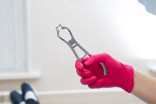 Zbliżenie dentysty ręka w czerwone rękawiczki medyczne. W ręku, narzędzie do montażu izolacji wycierania w ustach pacjenta — Zdjęcie stockowe