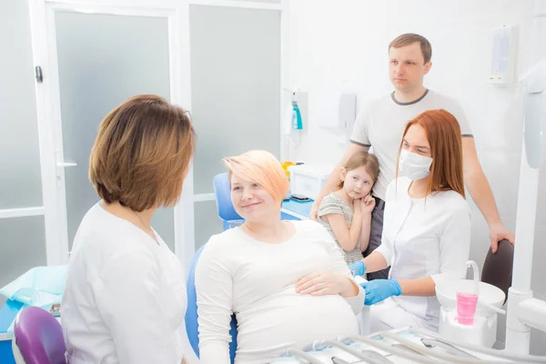 Zwangere vrouw bij de receptie bij de tandarts, de man en dochter zijn aanwezig in het kantoor. Tandheelkundige behandeling voor zwangere vrouwen — Stockfoto