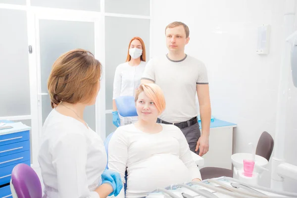 Zwangere vrouw bij de receptie bij de tandarts, de man zijn aanwezig in het kantoor. Tandheelkundige behandeling voor zwangere vrouwen — Stockfoto