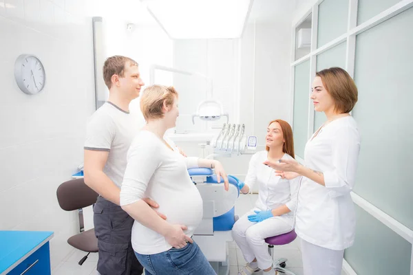 Zwangere vrouw en haar man communiceren met twee jonge vrouwen Tandartsen in een medisch kantoor. Tandheelkundige behandeling voor zwangere vrouwen — Stockfoto