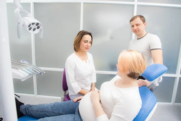 Беременная женщина и ее муж общаются с дантистом в медицинском кабинете. Лечение зубов беременным женщинам — стоковое фото