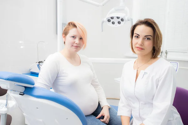 Positieve zwangere vrouw in tandartspraktijk, overleg met jonge vrouw tandarts. tandheelkundige behandeling voor zwangere vrouwen — Stockfoto