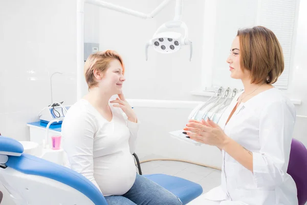 Positieve zwangere vrouw in tandartspraktijk, overleg met jonge vrouw tandarts. tandheelkundige behandeling voor zwangere vrouwen — Stockfoto