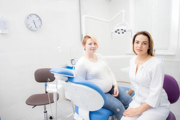 Positieve zwangere vrouw in tandartspraktijk, overleg met jonge vrouw tandarts. tandheelkundige behandeling voor zwangere vrouwen — Stockfoto