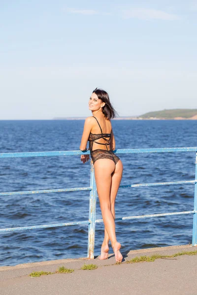 Joven sexy mujer en lencería está de pie en el muelle junto al mar — Foto de Stock