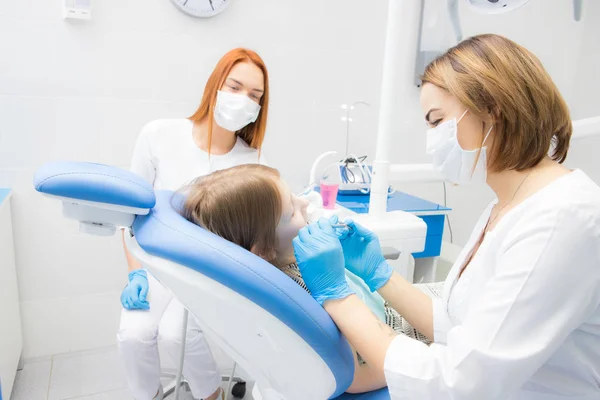 Una dentista y su asistente tratan los dientes de una niña —  Fotos de Stock