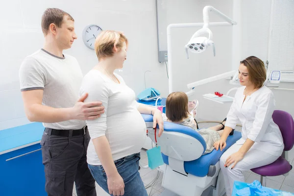 Een vrouwelijke tandarts communiceert met een kind en haar familie in een tandheelkundige kliniek. De moeder van het meisje is zwanger — Stockfoto