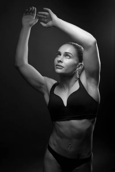 Zwart-wit foto van een jonge atletische vrouw sport bouwen in een badpak. Thema sport en bodybuilding. Een vrouw op een zwarte achtergrond handen omhoog — Stockfoto