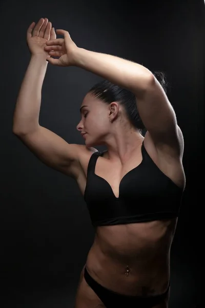 Foto de uma jovem atlética mulher esportes construir em um maiô. Esportes temáticos e musculação. Uma mulher em um fundo preto mãos para cima — Fotografia de Stock