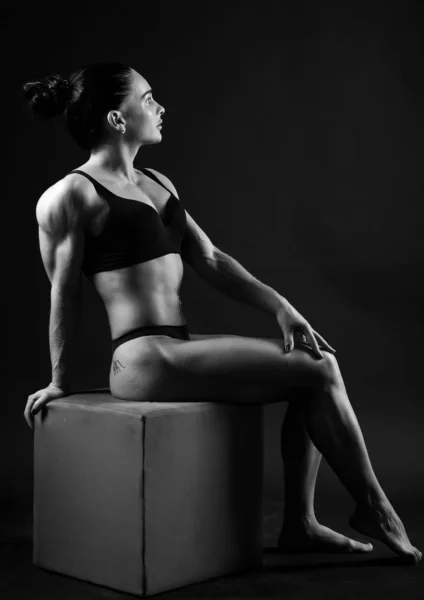 若い運動女子スポーツのモノクロ写真は水着で構築します。テーマスポーツとボディービル.完全な成長に戻って座っている黒い背景の女性 — ストック写真