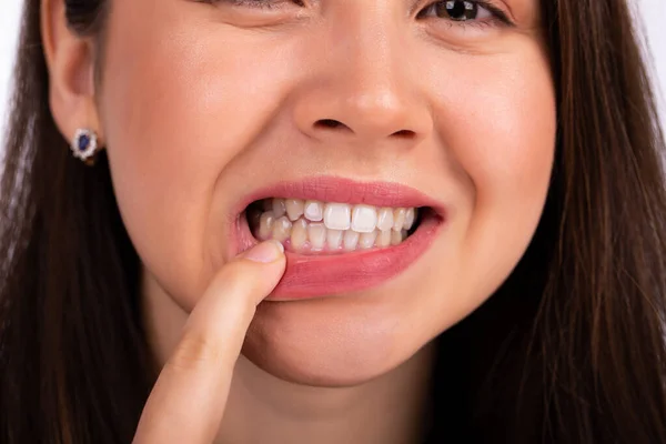 Młoda piękna kobieta dotyka zębów palcem na żuchwie, pokazując problem z zębami lub dziąsłami — Zdjęcie stockowe