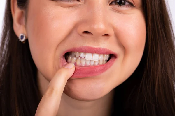 Mulher bonita jovem toca os dentes com o dedo na mandíbula inferior, mostrando um problema com dentes ou gengivas Imagem De Stock