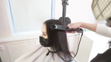 Keratin saç tedavisiyle uğraşan genç ve güzel bir kadın. Koruyucu maskeli genç bayan kuaför kuaförde çalışıyor.
