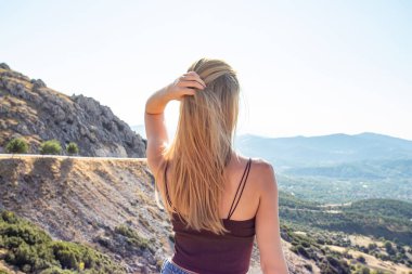 Genç, güzel sarışın kadın ufka bakıyor. Gezgin dağlarda duruyor.