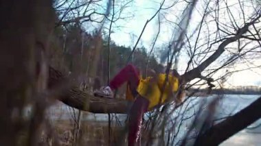 Yaroslavl, Rusya - Nisan 05, 2019. Sarı ceketli bir kadın baharda donmuş bir gölün yakınındaki bir ağaçta uzanıyor ve telefonundan selfie çekiyor..