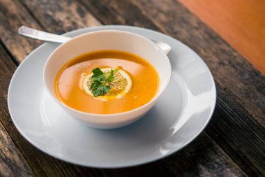 Bir dilim limon ve beyaz bir tabak içinde maydanoz ile mercimek kabak çorbası