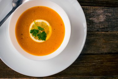 Bir dilim limon ve beyaz bir tabak içinde maydanoz ile mercimek kabak çorbası