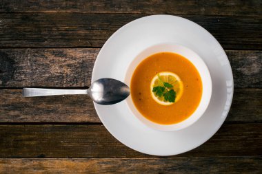 Bir dilim limon ve beyaz bir tabak içinde maydanoz ile mercimek kabak çorbası