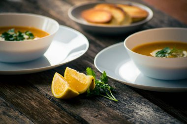 Bir dilim limon ve beyaz bir tabak içinde maydanoz ile mercimek kabak çorbası