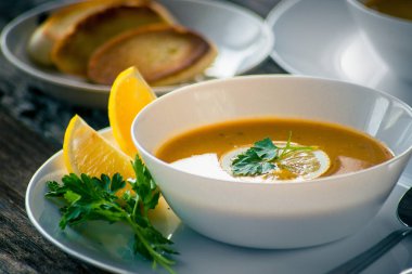 Bir dilim limon ve beyaz bir tabak içinde maydanoz ile mercimek kabak çorbası
