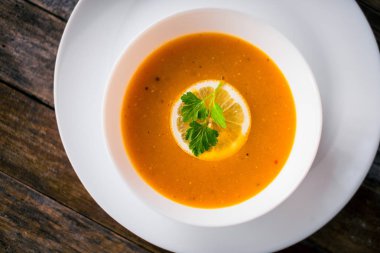 Bir dilim limon ve beyaz bir tabak içinde maydanoz ile mercimek kabak çorbası