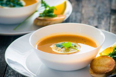 Bir dilim limon ve beyaz bir tabak içinde maydanoz ile mercimek kabak çorbası