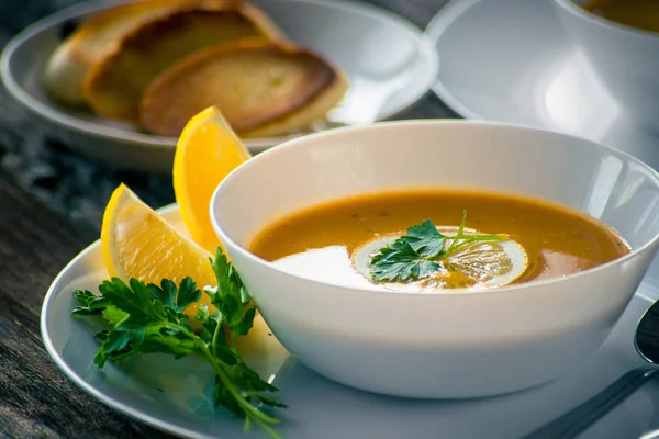 Bir dilim limon ve beyaz bir tabak içinde maydanoz ile mercimek kabak çorbası