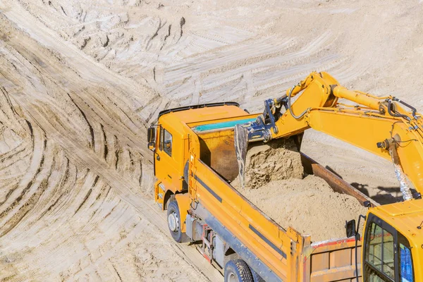 Work of the excavator and truck at a sand quarry. Excavator loading sand into a dump truck.