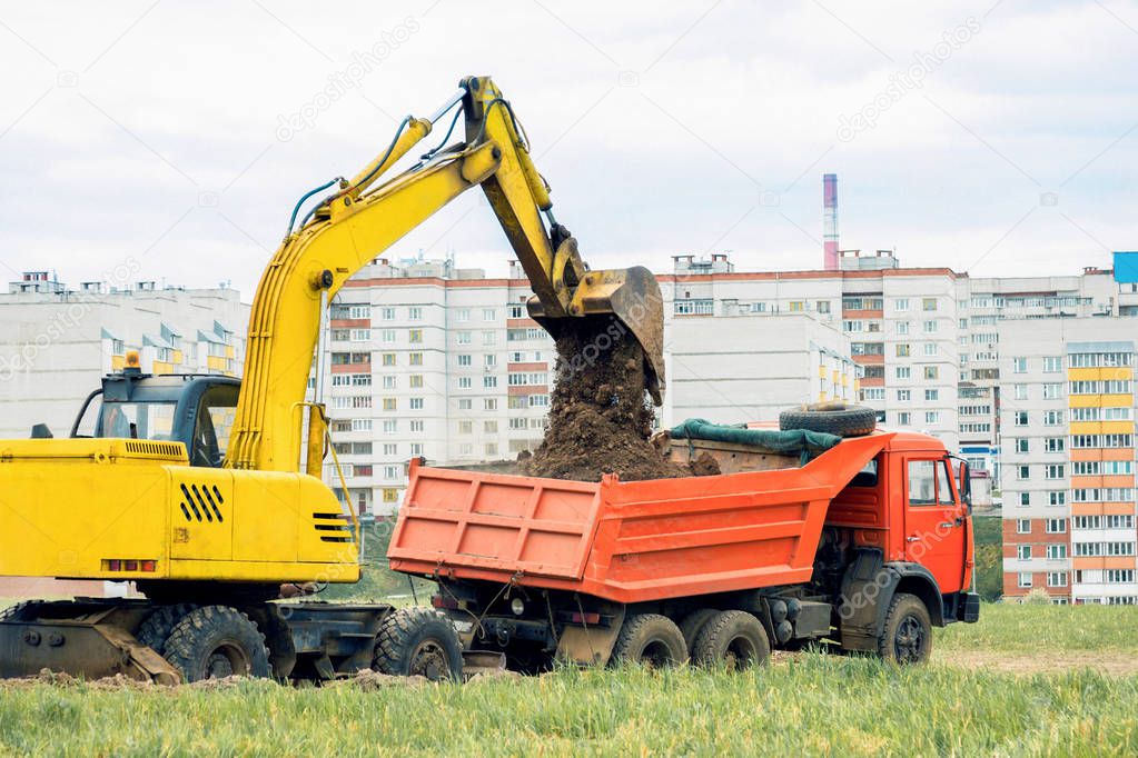 Excavator pours earth into a dump truck. Earthwork
