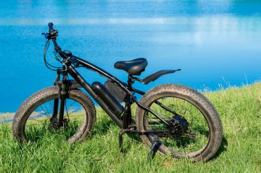 Gölün yanındaki çimlerin üzerinde kalın tekerlekleri olan siyah elektrikli bisiklet. Fatbike.