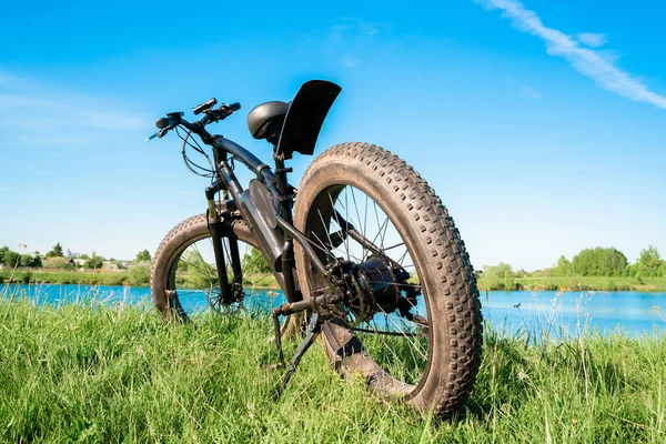 Gölün yanındaki çimlerin üzerinde kalın tekerlekleri olan siyah elektrikli bisiklet. Fatbike.