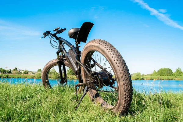 湖边草地上有厚重轮子的黑色电动车 胖子车 图库图片