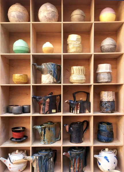 Cabinet with ceramic dishes. Kettle of unusual shape. Modern designer tableware. Round vases on the shelf. Large Wooden Shelves. Shelves with various dishes in the store