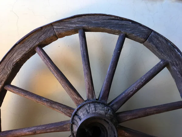 Wooden vehicle wheel against the background  light-brown color,a close up horizontally. Cracked wooden wheel of wain. Vintage wooden wheel in a rural court. Wooden boat/ship steering wheel hanging