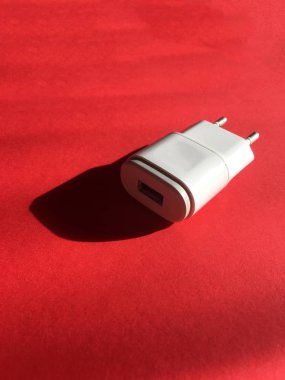 Arka planda kırmızı kağıt pastel beyaz renk adaptör fişi kadar kapatın. Teknoloji arka plan görünümü. Usb duvar şarj fişi kırmızı izole. Konektör fişi. Usb bağlantı noktasına elektrik adaptörü