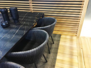 Yarım daire sandalye ve siyah mermer masa. Tropikal İç tarzı. Ahşap panellerin bölünmesi. Ahşap zemin. Örgü sandalyeler. Masadaki dekor