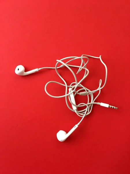 Kırmızı arka plandaki kulaklıklar, kulaklıkların kabloları birbirine dolanmış durumda. Karışık kablolu beyaz akıllı telefon kulaklıkları