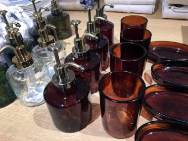 Mağazada ahşap bir rafta banyo aksesuarları. Mağaza rafındaki jenerik sabunluklar. Sıvı sabun için cam dağıtıcılar. Banyo için iç mekan eşyaları. Hırdavat çırağı