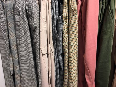 Dükkandaki bir tezgahın üzerinde asılı bir sıra kıyafet. Giysi arka plan grubunu kapatın. Moda tasarım konsepti. Askıları bir mağazada güzel renkli giysiler. Renkli pantolon bir mağaza tezgahında asmak
