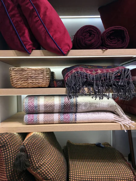 Stack of blankets and pillows are on the shelf. Folded winter clothes on shelves in wardrobe. Towels for sale in store that sells bed, table and bath articles. Merchandise arranged in shop interior