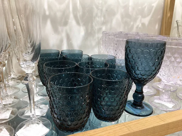 Dark blue Water Glasses Vintage-inspired Pattern. Glasses and stemware set. Designer glassware on a glass shelf in a store. Colorful vintage Glassware. Various Types Of colorful set tableware