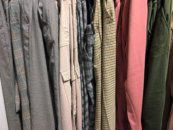 店内のカウンターにぶら下がっている服の列 服の背景のグループをクローズアップ ファッションデザインコンセプト ハンガーの上の店で美しいカラフルな服 店のカウンターに色のズボンが掛かる — ストック写真
